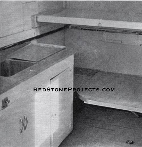 This is an interior view of the trailer looking forward, with the front bunk in place and single bed arrangement made by lowering the table down to the same level as the dining nook seats.
